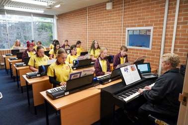 Classroom of students and teacher learning how to play a piano keyboard