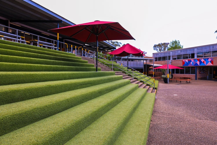 Steps covered with artificial grass with red umbrellas in school courtyard