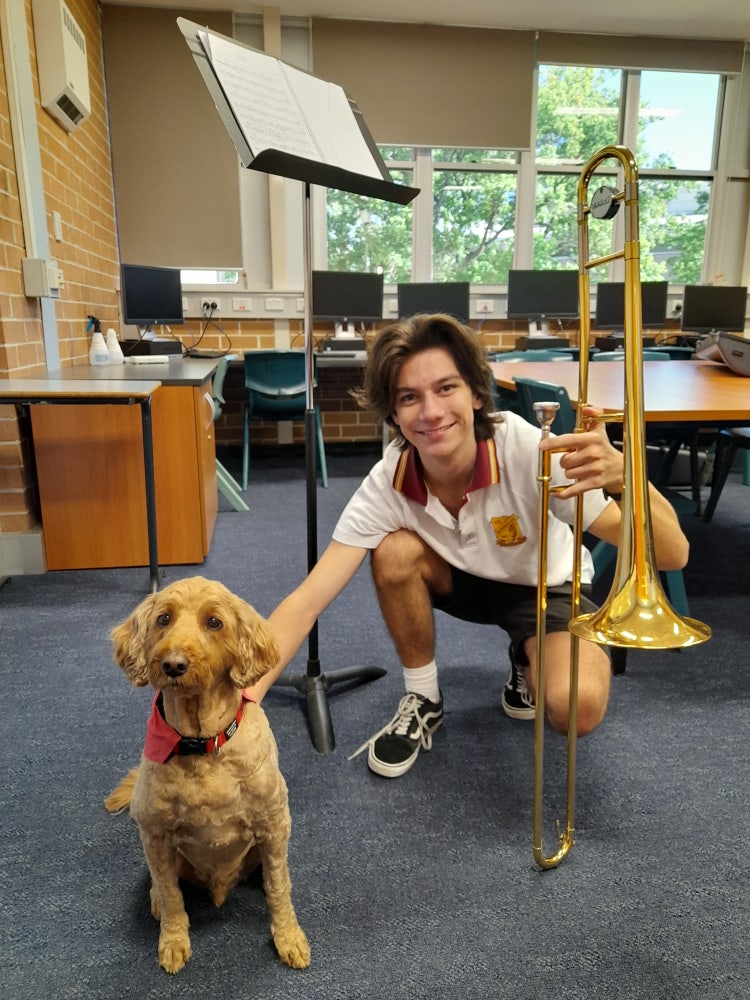 Male student with trombone patting school support dog.
