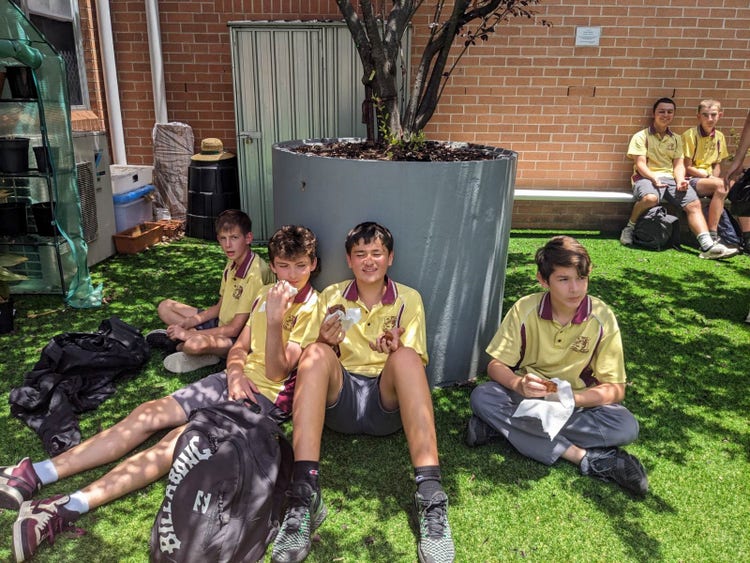 A group of boys sitting on grass in front of a tree