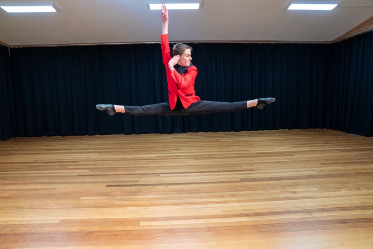 A person in a red shirt and black pants doing a split in the air